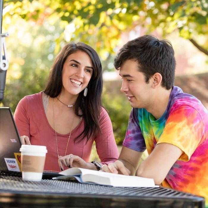 Two students talking at table outside